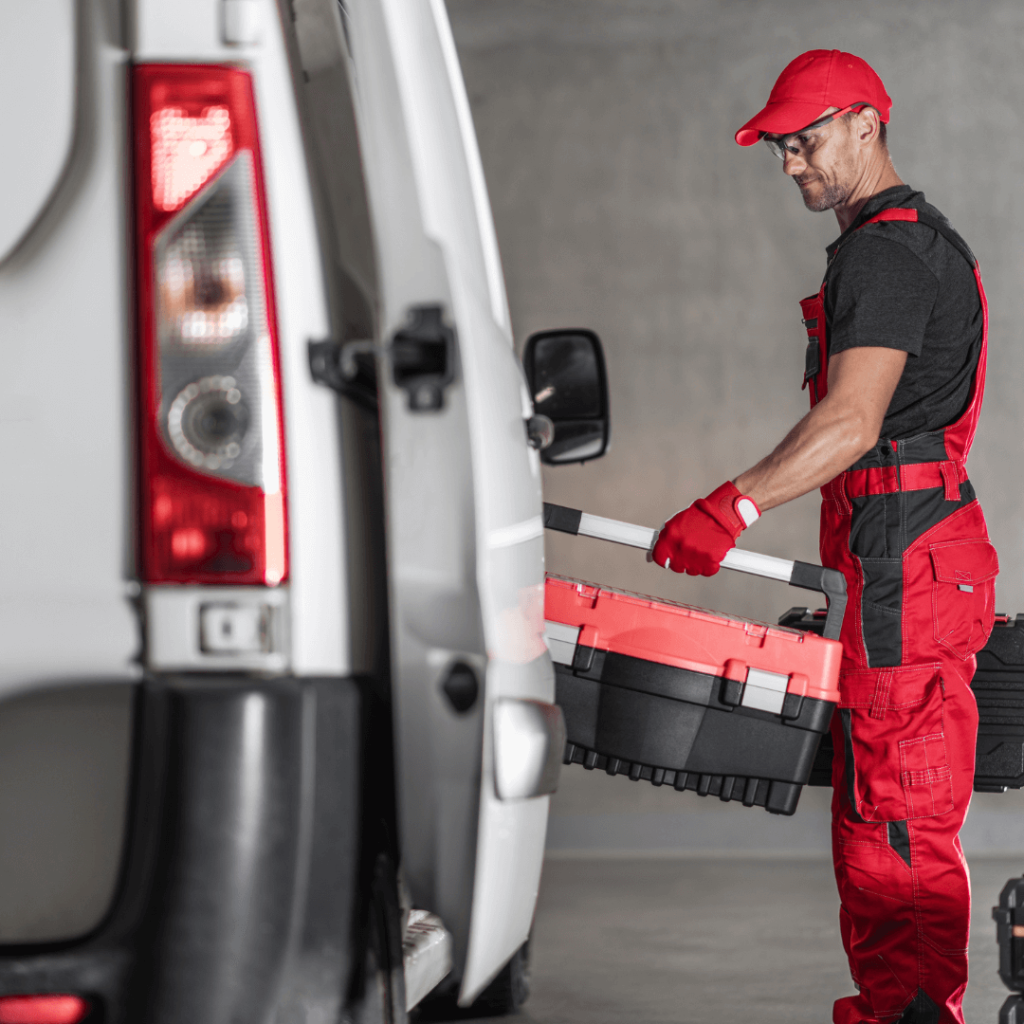 Vehicle technician in red overalls stood next to a commercial van with a toolbox